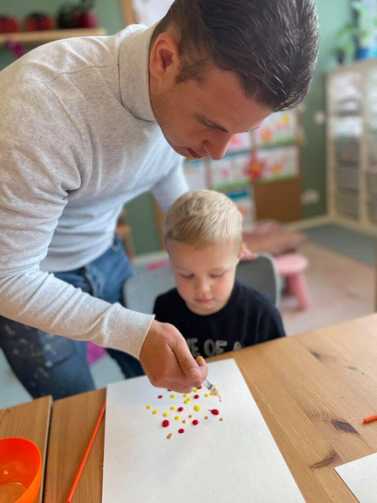 Een pedagogisch medewerker helpt een kind met verven op de bso